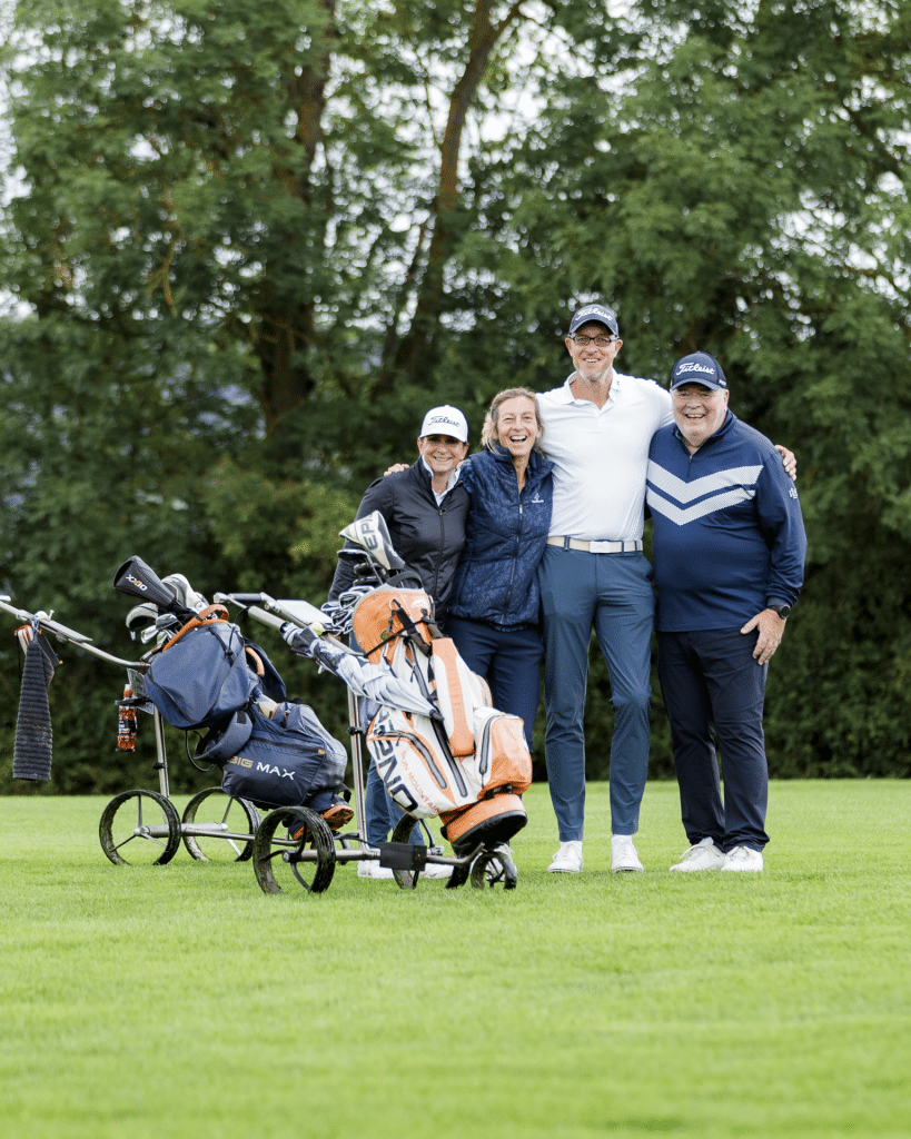 ier Teilnehmer eines Flights posieren lachend mit Golftrolleys und Golfbags auf dem Fairway beim Charity-Golfturnier von Round Table 98 Bayreuth