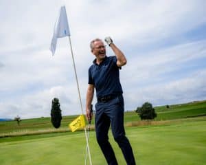 Golfspieler jubelt mit geballter Faust am Grün neben der Fahne nach einem gelungenen Putt beim RT 98 Golfturnier.
